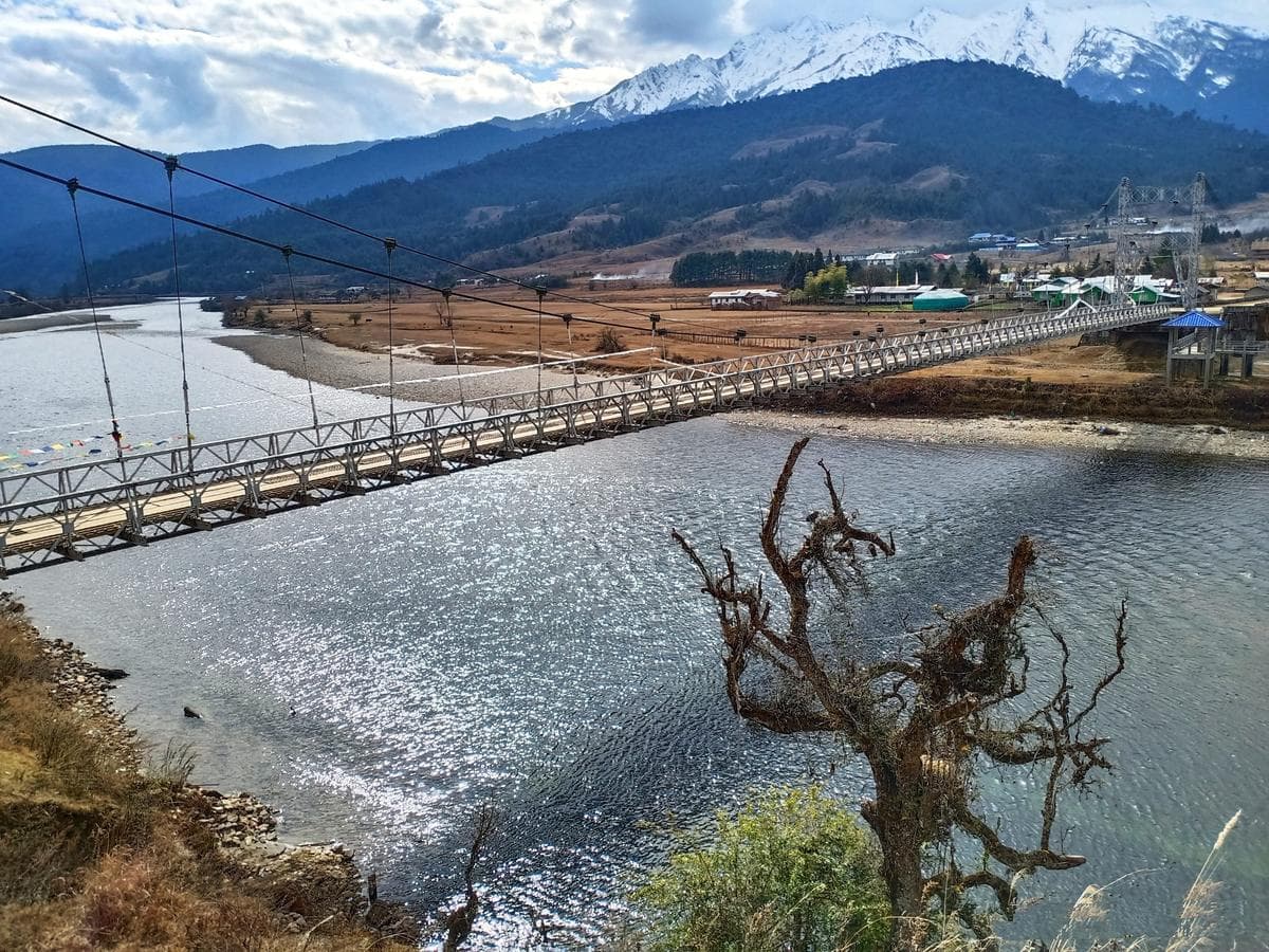 Snow-capped mountains and traditional wooden houses along the Yargyap Chu River in Mechuka Valley, Arunachal Pradesh